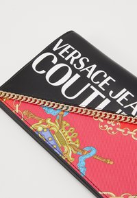 Portafoglio nero e rosso di Versace con un accento in catena d'oro. Presenta lettering bianco audace e un motivo decorativo con corone e simboli.