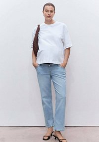 Camiseta blanca de algodón, corte relajado, combinada con jeans rectos de mezclilla azul claro. El modelo lleva un bolso de hombro marrón oscuro y sandalias negras.