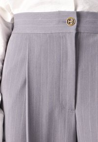 Pantalons gris à rayures fines avec taille haute, plis et fermeture à bouton doré. Le tissu a l'air lisse avec un design ajusté.