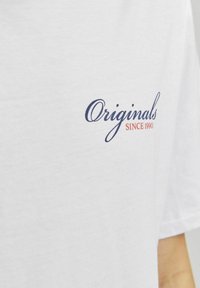 Bijela pamučna majica s mornarskoplavim kursev tekstom "Originals" i narančastim logom "SINCE 1990". Kratki rukavi i opušteni kroj.