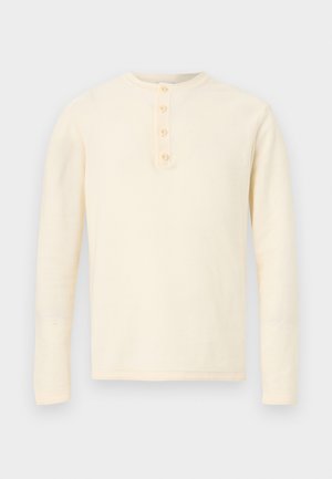 Chemise henley crème à manches longues avec quatre boutons sur la patte de boutonnage avant, présentée sur un fond blanc.