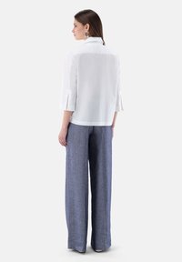 White collared blouse with three-quarter sleeves paired with loose-fitting blue linen pants, showcasing a clean and minimal design.