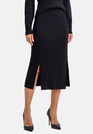 Schwarz gerippter knielanger Rock mit seitlichen Schlitzen, aus einem strukturierten Strickmaterial, kombiniert mit glänzenden schwarzen Highheels.