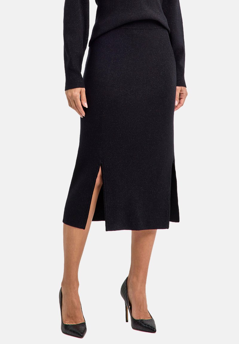 Zwarte geribbelde rok tot op de knie met zijsplitten, gemaakt van een gestructureerde breimateriaal, gecombineerd met glanzende zwarte hoge hakken.