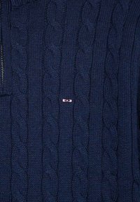 Pull en maille bleu marine avec motif en cable, doté d'un col zippé et d'un petit logo rose sur la poitrine.
