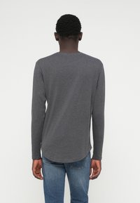 Grijze T-shirt met lange mouwen, slim fit, gemaakt van zacht materiaal, met een ronde zoom en een minimalistisch ontwerp, gecombineerd met blauwe spijkerbroek.