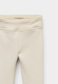 Beżowe legginsy o gładkiej fakturze, z wysokim stanem i minimalnymi detalami szwów. Nazwa marki "CALZEDONIA" widoczna wewnątrz pasa.