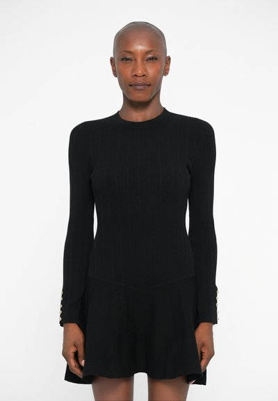 Vestido negro de manga larga, con textura acanalada en el torso, falda acampanada y detalles de botones dorados en los puños de las mangas. Silueta clásica y ajustada.