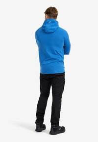 Blå huvtröja i mjukt material, kombinerad med svarta cargobyxor. Funktioner inkluderar en justerbar huva och fickor med dragkedja.