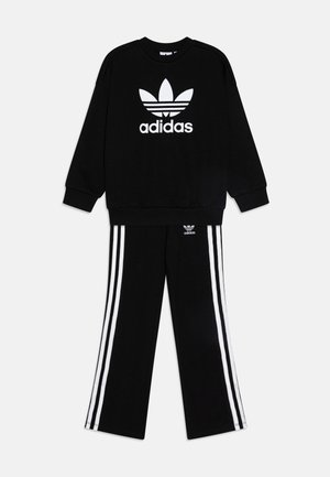 Černá mikina Adidas s bílým logem na přední straně, spárovaná s černými kalhotami se třemi bílými pruhy na každé nohavici.