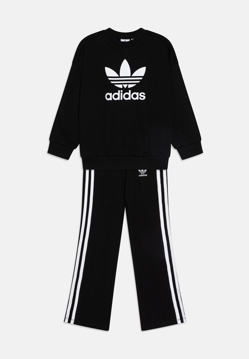 Črna Adidas kapuca z belim logotipom na sprednji strani, v kombinaciji z črnimi hlačami, ki imajo tri bele črte po vsaki nogi.