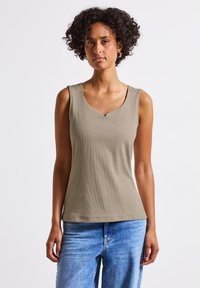 Ärmlös olivgrön topp med ribbad struktur, med en V-formad halsringning och en avslappnad passform. Kombinerad med ljusblå jeans.