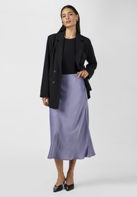 Svart skräddarsydd kavaj över en figurnära svart topp, i kombination med en flödande lavendelfärgad satinkjol och spetsiga svarta klackar. Slät textur, elegant design.