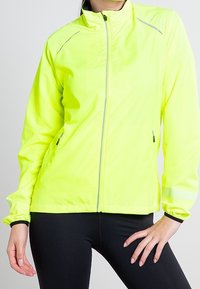 Žlutá větrovka s vysokou viditelností, se zipem, reflexními detaily a bočními kapsami. Lehký materiál a elastické manžety.