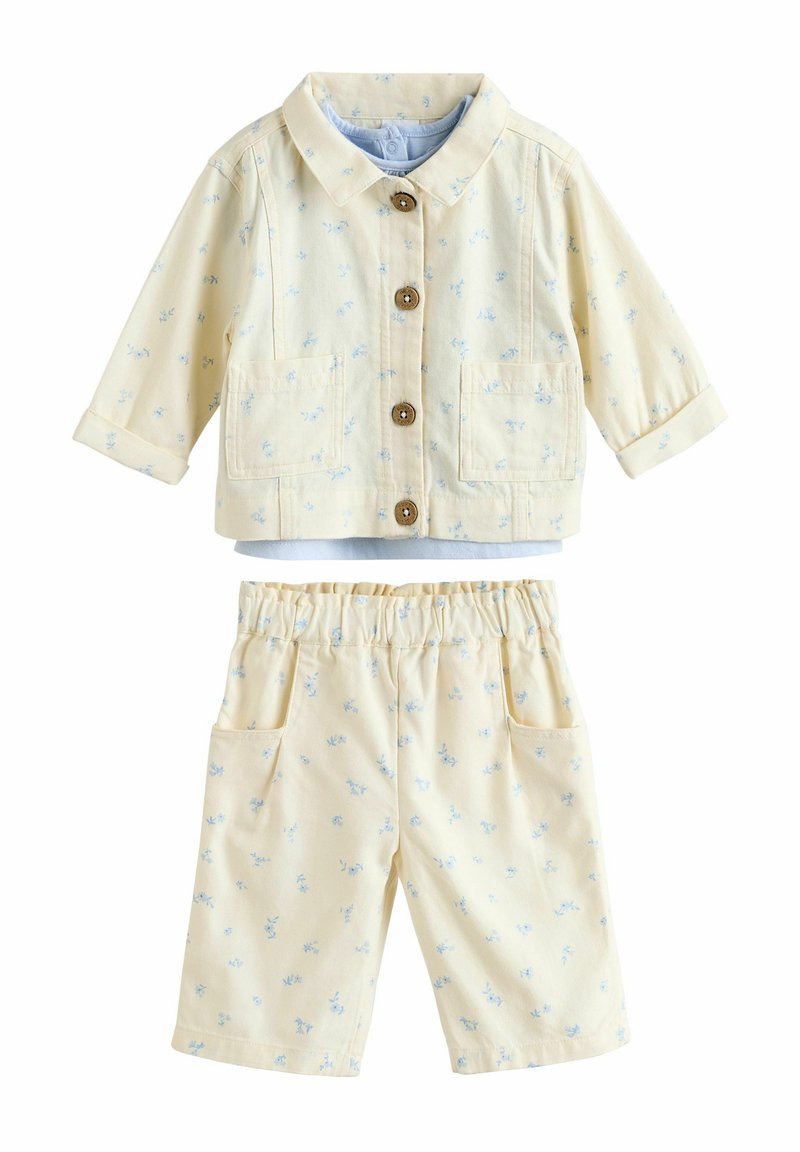 Costum format din două piese, de un galben deschis, ce include o jachetă cu guler, dotată cu nasturi din lemn și pantaloni scurți asortați, ambele decorate cu un mic model floral albastru.