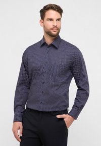 Camicia con bottoni in tessuto blu navy con piccoli pois bianchi e rossi. Presenta un colletto appuntito, maniche lunghe e una vestibilità aderente.