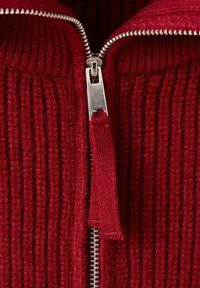 Roter, gerippter Pullover mit durchgehendem Reißverschluss aus silbernem Metall und einem Stoffzugband. Die Textur ist weich, mit engem Sitz und auffälligem Strickmuster.