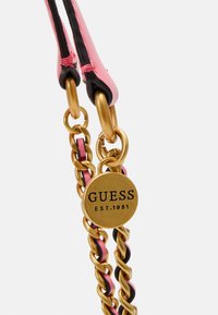 Sangles en cuir rose et noir avec des accents de chaîne en ton or ; comprend une étiquette ronde en or portant l'inscription "GUESS EST.1981". Construction durable.