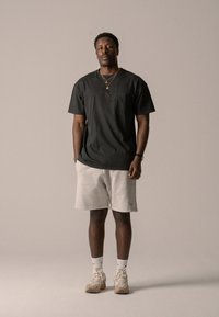 Svart kortermet skjorte med brystlomme, kombinert med lysegrå shorts. Tilbehør inkluderer lagdelte gullkjeder og beige joggesko.