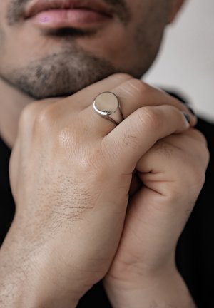 Silver-colored ring with a smooth, round top, worn on the index finger of a hand with light skin and visible hair texture.