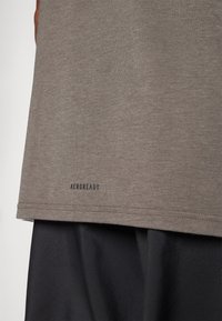 Grey athletic shirt with a soft texture, featuring a rounded hem and a black "AEROREADY" logo at the lower edge. Layered with black shorts.