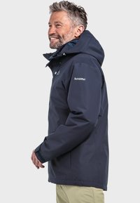 Navy wasserfeste Jacke mit Kapuze, verstellbaren Manschetten und Reißverschlüssen. Merkmale sind ein Logo auf der Brust, atmungsaktives Material und eine lockere Passform.