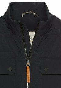 Granatowa pikowana kurtka z wysokim kołnierzem, zamkiem błyskawicznym z skórzaną pętelką oraz dwiema kieszeniami z klapą z zapięciem na napy.