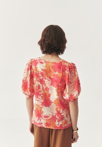 Lillelillel blouse, millel on erksad roosa ja oranži muster, lühikesed puff-sleeve'id ja kerge kangas, kantud pruunide pükstega.