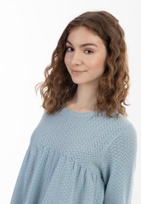 Lyseblå tekstureret sweater med mønstret buste og samlet kant. Stoffet ser blødt ud, med en afslappet pasform og rund halsudskæring.