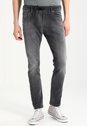 Men's black denim jogger pants with a drawstring waist, slim fit, faded texture, and contrasting stitching details. Styled with white sneakers.