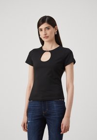 Musthave musta lühikeste varrukatega topp, millel on kaeluse piirkonnas võtmeaugu lõige, sile tekstuur ja keha lähedane lõige. Kombineeritud tumehallide kulutatud teksadega.