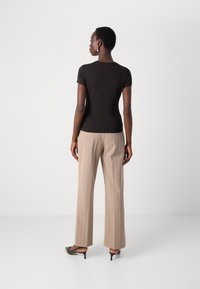 T-shirt aderente nero abbinato a pantaloni beige a righe larghe. Tessuto strutturato con un aspetto liscio. Scarpe col tacco nere completano l'outfit.