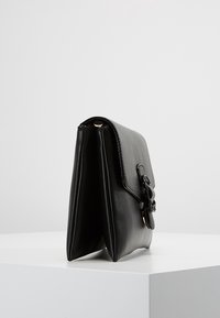 Sac à main en cuir noir au design structuré, texture douce et fermeture à rabat. Présente des accents en métal sur le côté et un profil élégant.