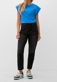 Niebieska koszulka z krótkim rękawem, czarne jeansy o wysokim stanie i białe sneakersy z zielonymi akcentami. Casualowy, dopasowany krój o gładkiej fakturze.