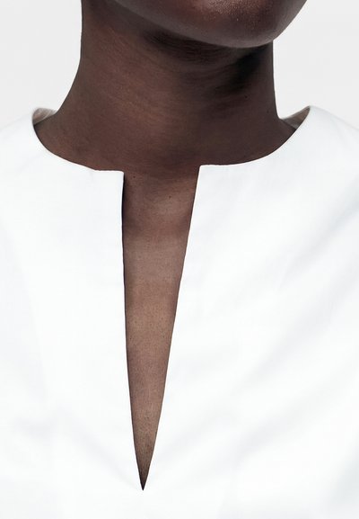 Gros plan d'une personne portant un haut blanc avec une encolure fendue profonde à l'avant, montrant le cou et le haut de la poitrine.