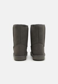 Grå mocka ankelstövlar med mjukt foder, rund tå och texturerade gummisålar. Bakom bilden syns sömnadsdetaljer och en slät finish.