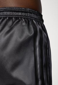 Sorte satinshorts med elastisk talje, med sidelængder og en glat tekstur. Designet er strømlinet og tætsiddende.