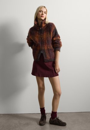Giacca zip-up in misto lana multicolore con colletto alto, silhouette over size e texture a fantasia, abbinata a una gonna marsala.