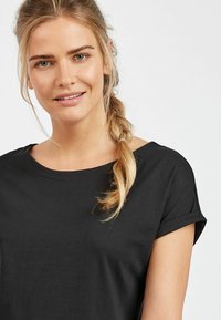 Svart kortärmad t-shirt med rund halsringning och uppvikta ärmar, tillverkad av mjukt bomullstyg, med en avslappnad passform.