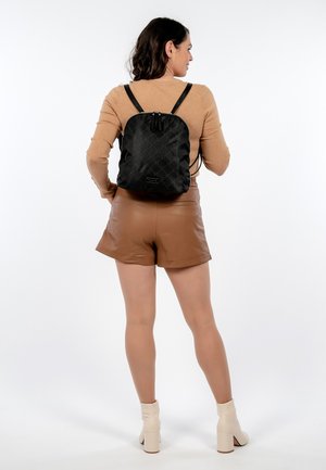 Schwarzer gesteppter Rucksack mit runder Form, ausgestattet mit verstellbaren Trägern und einem Reißverschlussverschluss. Glatte Textur, minimalistisches Design.