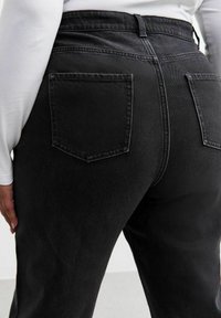 Pantalones de mezclilla negros de talle alto con dos bolsillos traseros, textura suave y un diseño ajustado. La cinturilla cuenta con detalles de pasadores para cinturón.