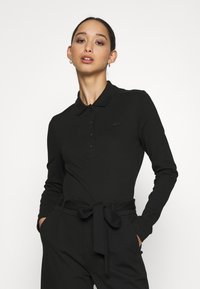 Polo shirt nero a maniche lunghe, con bottoni e un logo discreto sul petto. Tessuto liscio con un design aderente.