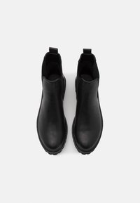 Bottines en cuir noir avec languettes, bouts arrondis et semelles épaisses en caoutchouc, vues de dessus sur fond blanc uni.