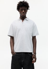 Grå polo t-shirt med krave og korte ærmer. Lavet af blødt stof, har en v-hals åbning og en afslappet pasform. Bæres med mørke denimbukser.