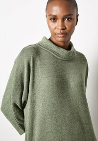Maglione verde a maglia con un colletto alto e piegato e maniche larghe. Il tessuto presenta un motivo strutturato e a coste, con una vestibilità ampia.