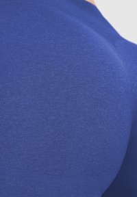 Tessuto blu aderente che mostra una superficie liscia con una leggera lucentezza. Il materiale appare elastico, enfatizzando le linee del capo.