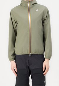 Ljus olivgrön lättviktsjacka med dragkedja och huva, med en kontrasterande gul och silverdragkedja, elastiska ärmslut och en broderad logotyp.