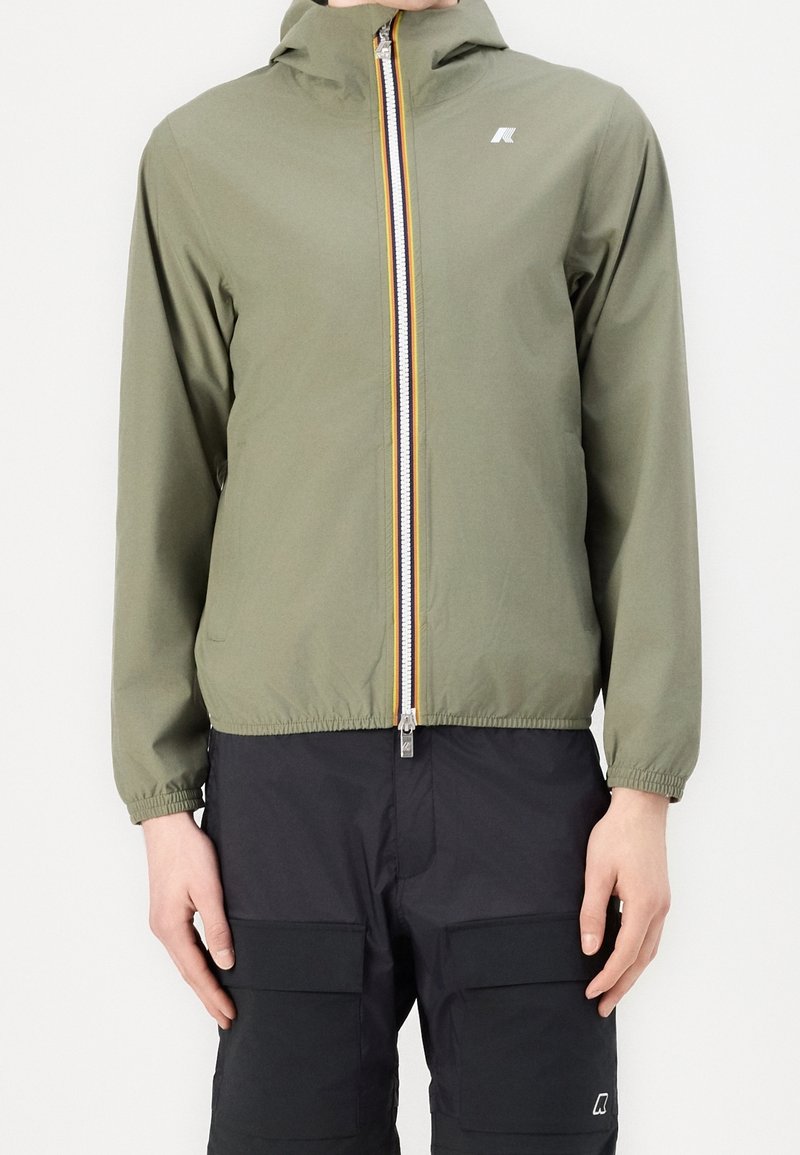 Ljus olivgrön lättviktsjacka med dragkedja och huva, med en kontrasterande gul och silverdragkedja, elastiska ärmslut och en broderad logotyp.