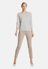 Hellgrauer gestrickter Pullover mit dreiviertel Ärmeln, kombiniert mit beigen Slim-Fit-Hosen und spitzen weißen Heels. Glatte Textur und klare Linien.