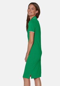 Grünes Polo-Kleid aus Baumwolle, schmal geschnitten mit kurzen Ärmeln und weißem Kragenrand. Mit einem seitlichen Schlitz nahe dem Saum.